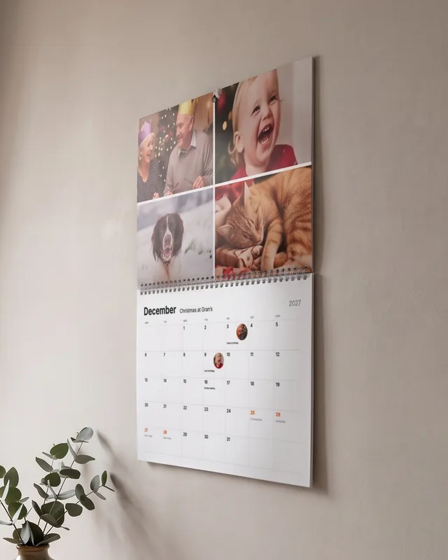 A photo calendar open at December, with four Christmas photos, hanging on a hallway wall