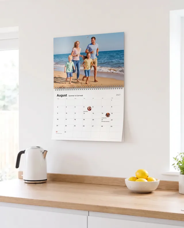A photo calendar of a family on a beach, hanging on a white kitchen wall