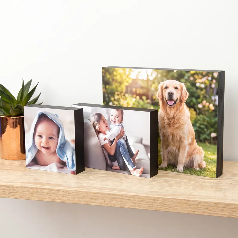 Three black-edged wooden photo blocks in different sizes on a pale oak shelf