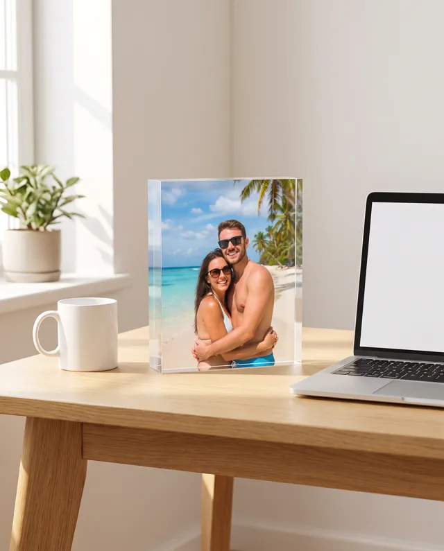 An acrylic photo block of a couple on holiday, standing on a desk beside a mug and laptop