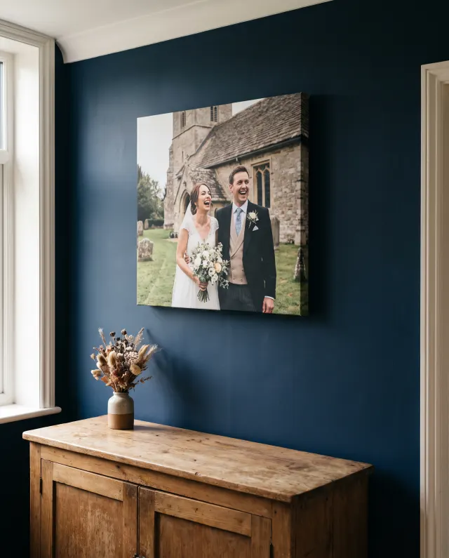 A canvas print of a bride and groom laughing outside a church, on a navy hallway wall