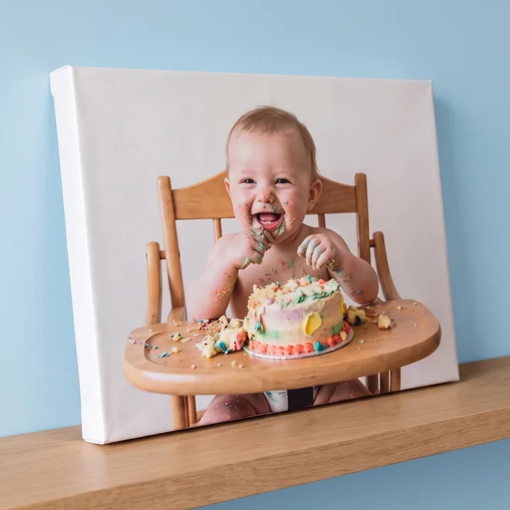 A canvas print of a laughing baby covered in birthday cake, leaning on a shelf against a pale blue wall