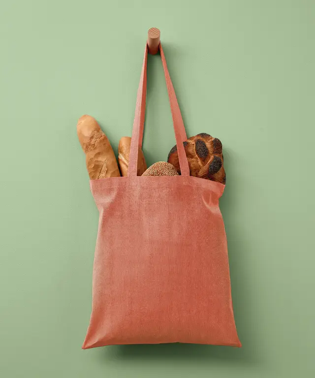 An orange marl recycled cotton tote bag hanging from a peg, filled with fresh bread