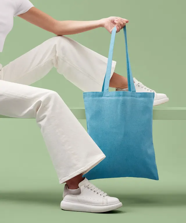A sky blue marl recycled cotton tote bag held at knee height by someone sitting on a bench