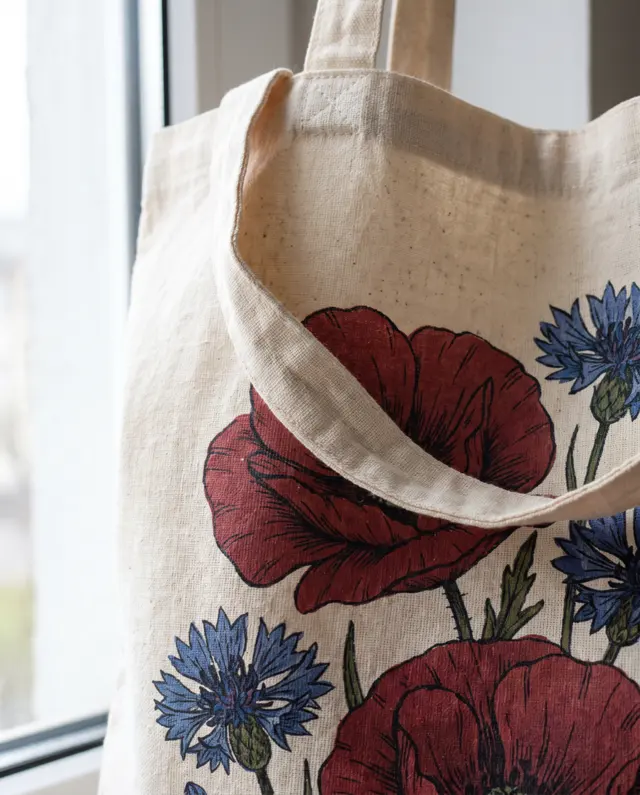 Close up of a full colour print of poppies and cornflowers on a natural cotton tote bag, the cotton weave showing
