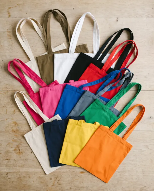 Cotton shopper tote bags in all twelve colours, fanned out on an oak table